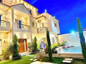 A multi-story hotel with a swimming pool, outdoor lighting, and a well-maintained garden.
