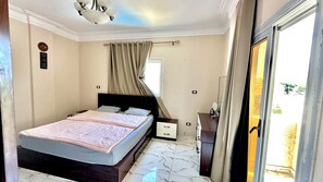 A bedroom with a bed, a nightstand, a dresser, and a window with curtains. - Luxury Villa (Alexandria)