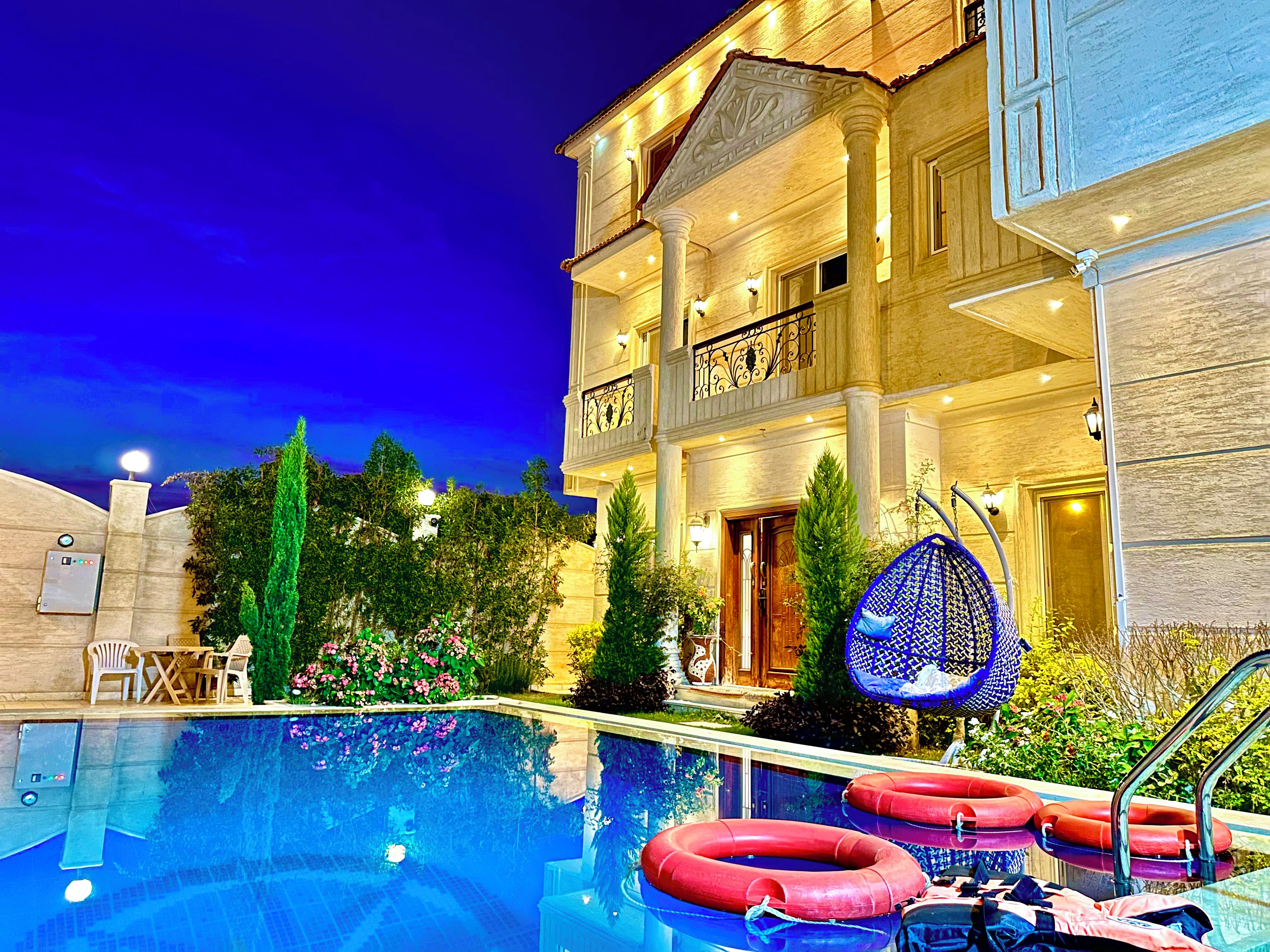 A hotel with a swimming pool, outdoor seating, and a well-lit entrance.