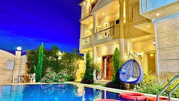 A hotel with a swimming pool, outdoor seating, and a well-lit entrance.