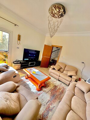 A living room with a sofa set, a coffee table, a television, and a chandelier.