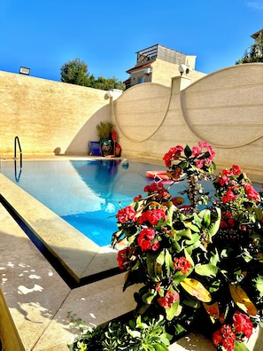 Una piscina con pared curva y un parterre con flores rojas.