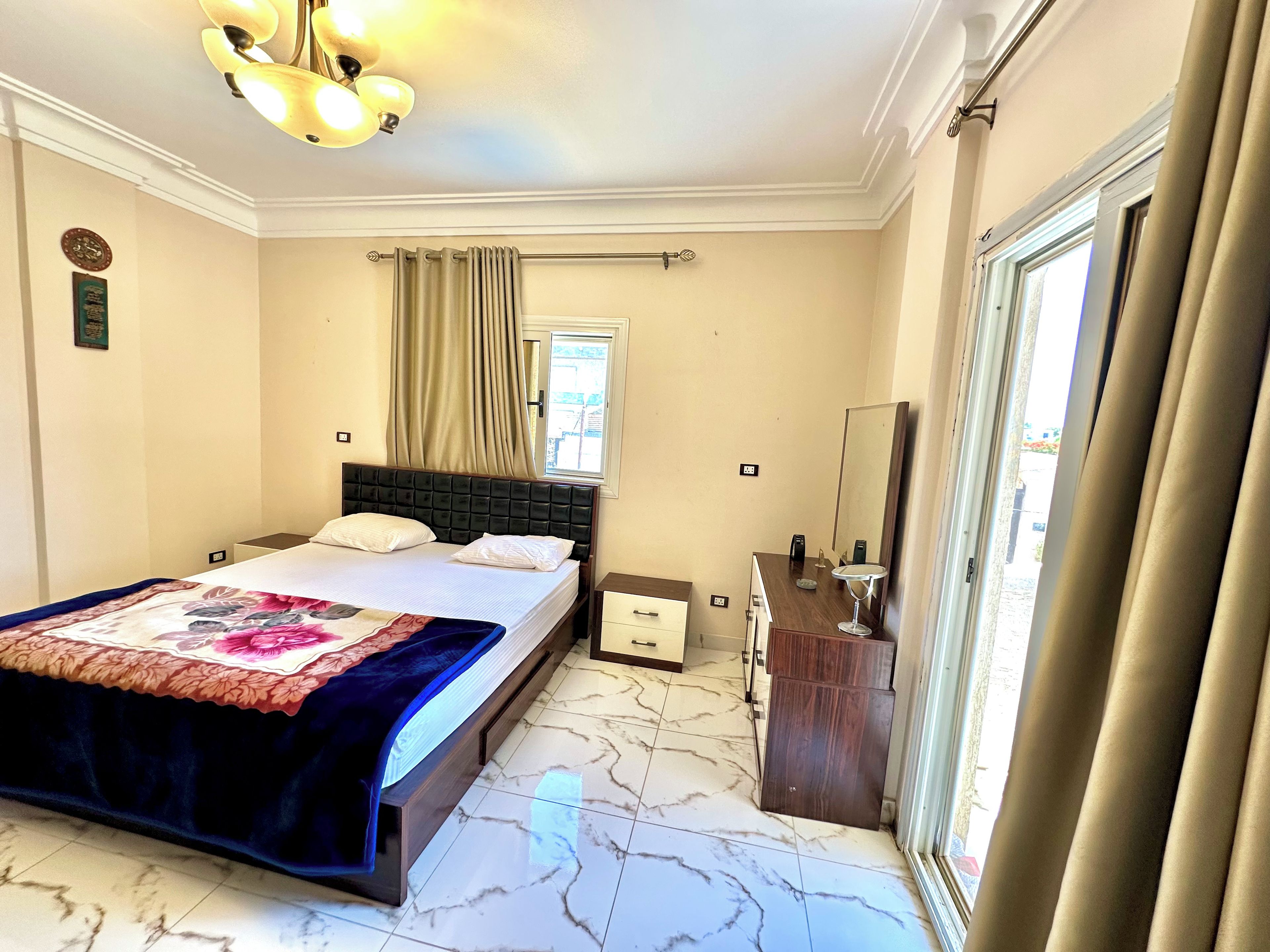 A hotel room with a bed, bedside table, mirror, and a window with curtains.