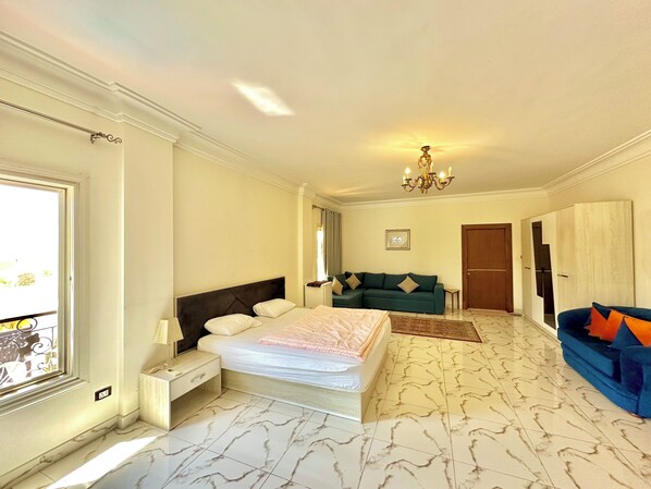 A hotel room with a bed, a sofa, a chandelier, a door, and a window.