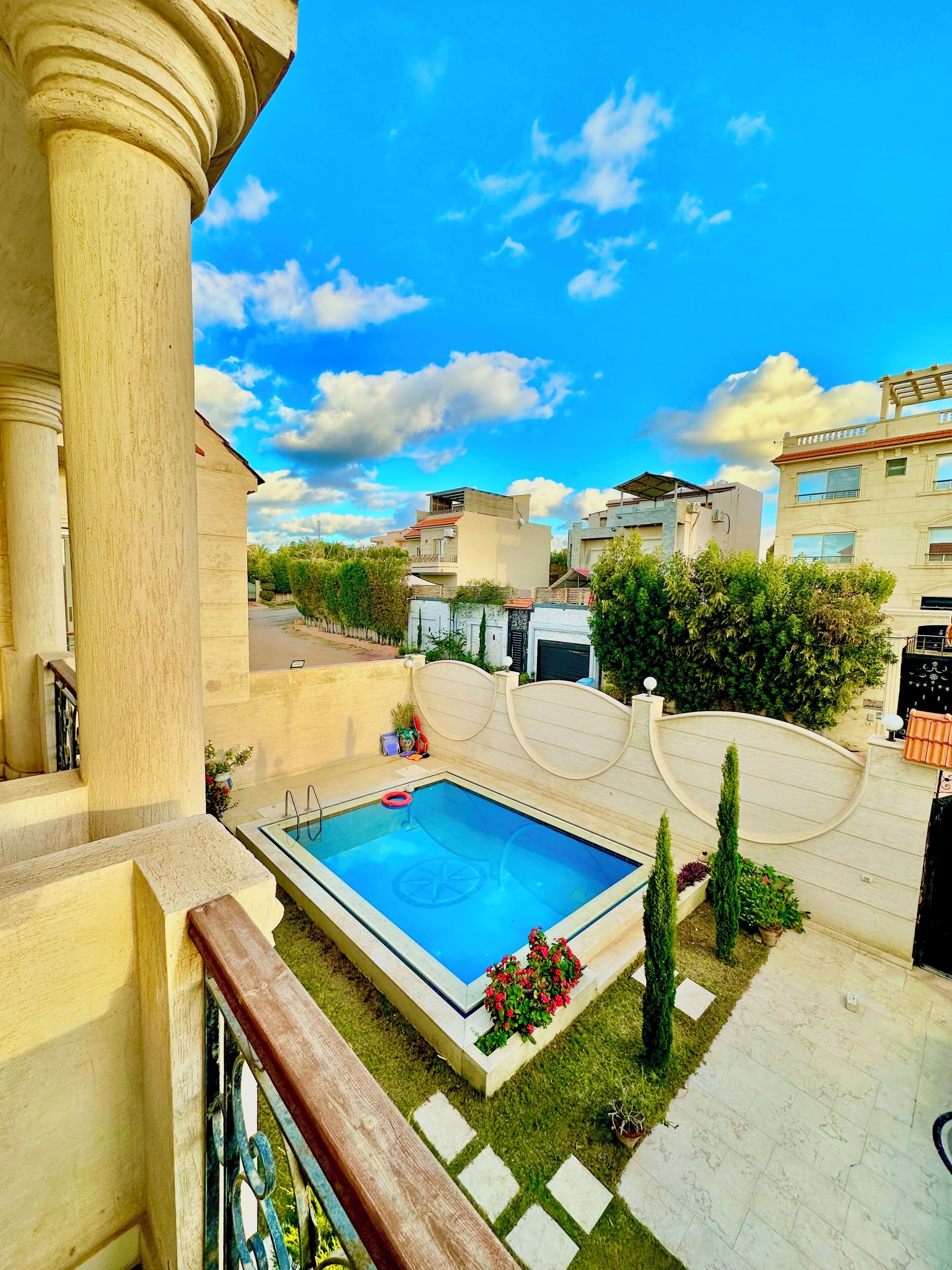 A residential area with a swimming pool, a well-maintained lawn, and modern buildings in the background.