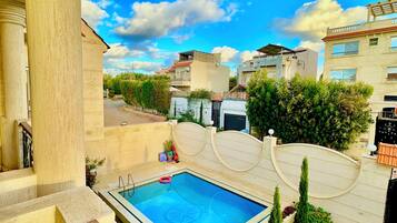 A residential area with a swimming pool, a well-maintained lawn, and modern buildings in the background.