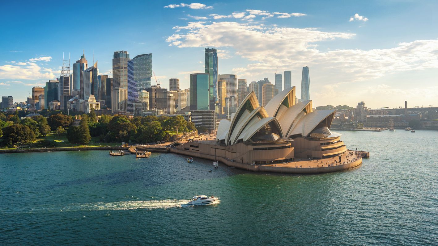 A city skyline with modern buildings and the Sydney Opera House by the waterfront.