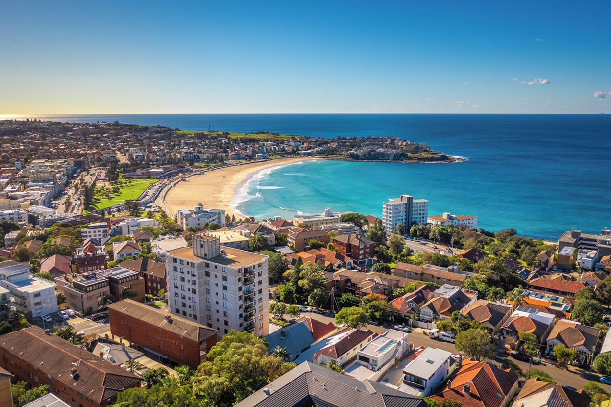 A coastal cityscape with a beach, residential buildings, and a clear sky.