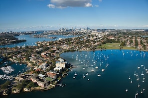 Vue aérienne d’une ville côtière, avec un port de plaisance rempli de bateaux, des quartiers résidentiels et, au loin, le profil de la ville.