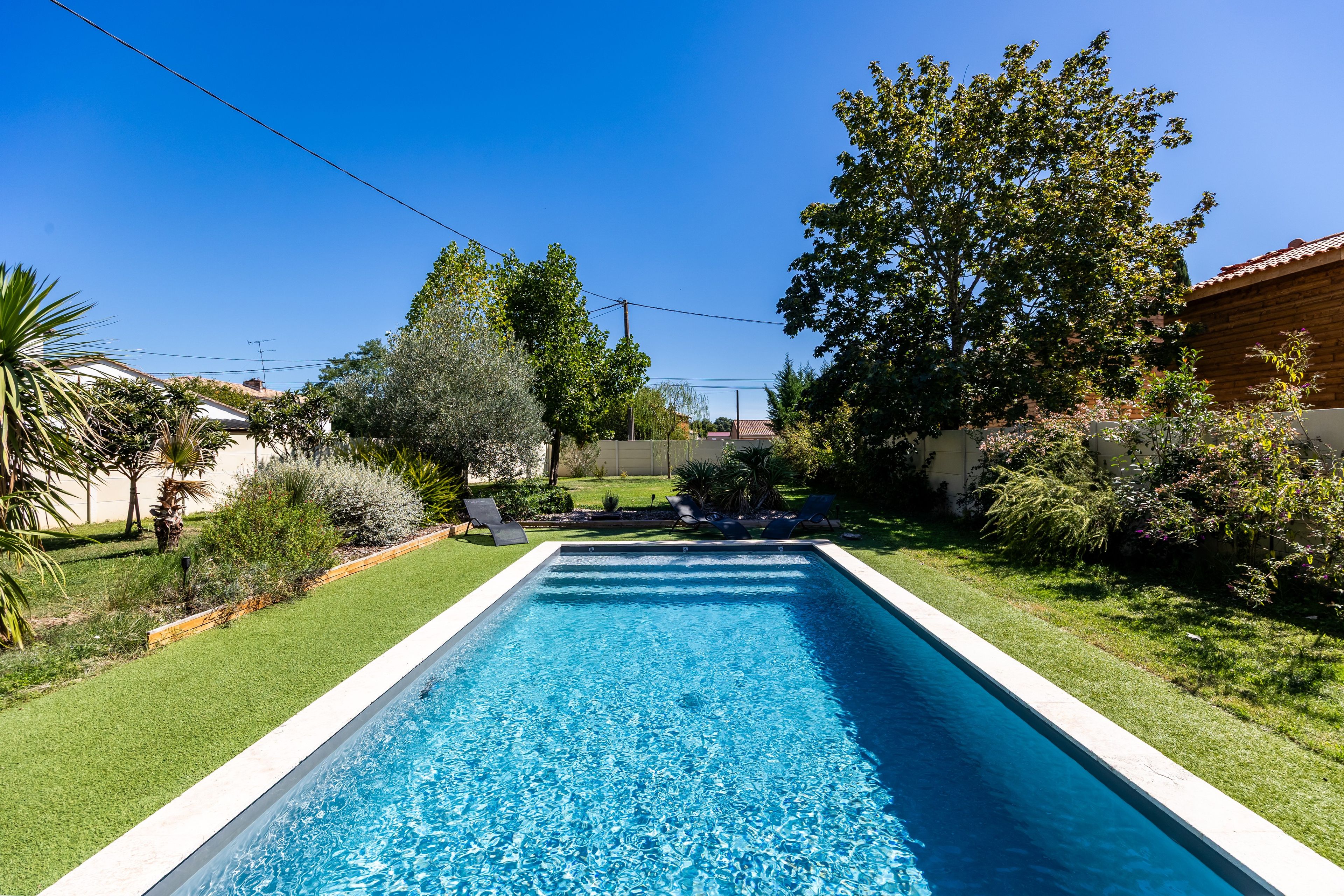 Una piscina rectangular con agua cristalina, rodeada de un césped cuidado y diversos arbustos.