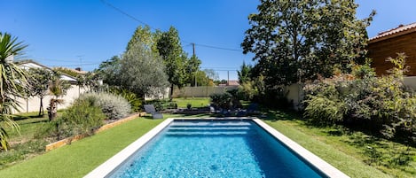 Una piscina rectangular con agua cristalina, rodeada de un césped cuidado y diversos arbustos.