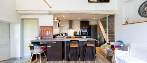 Una cucina moderna con isola centrale, sgabelli da bar, tavolo da pranzo e una scala che conduce a un piano superiore.