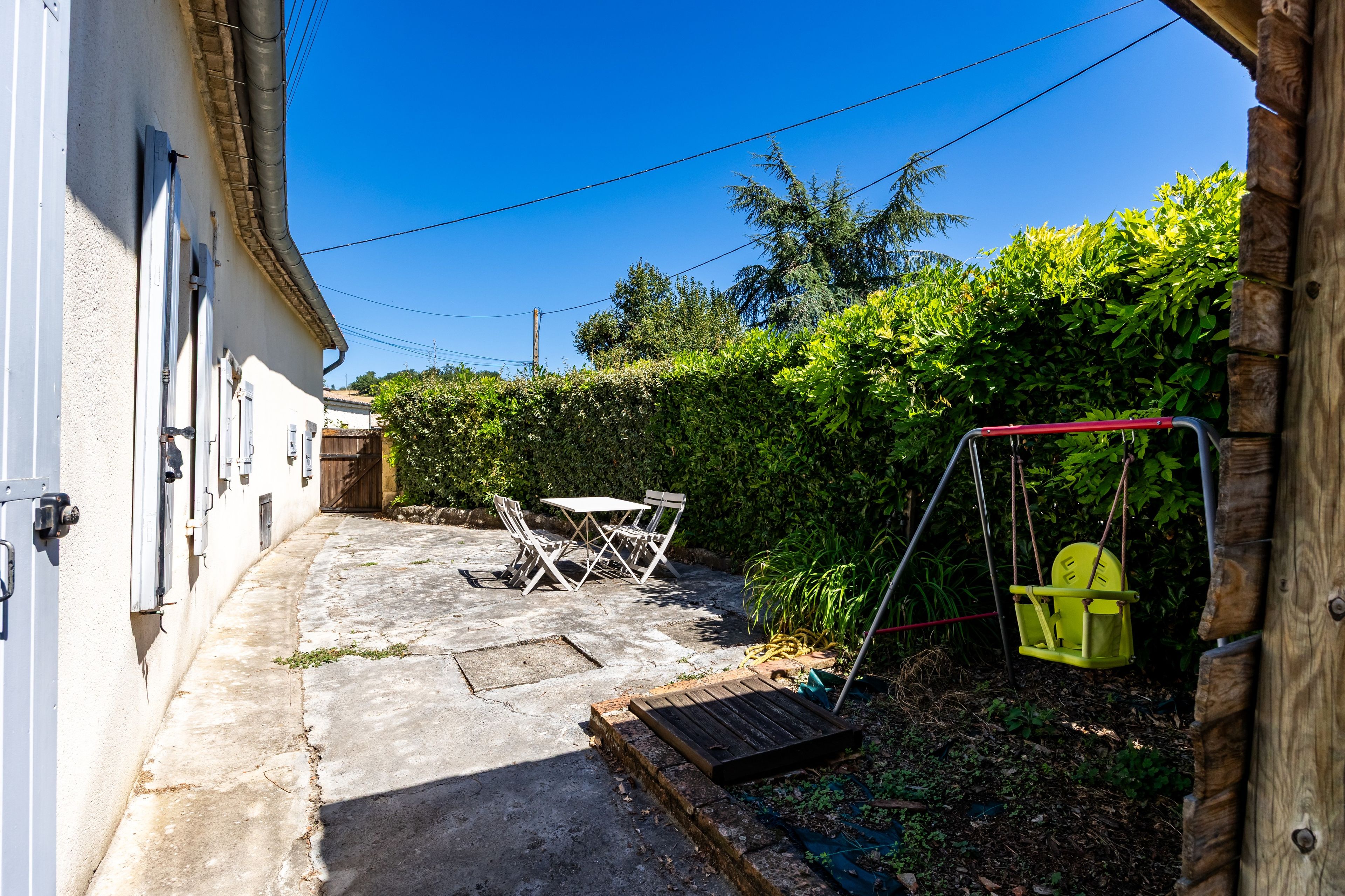 Une petite cour avec une balançoire, une table et des chaises, et une porte en bois sur le côté gauche.