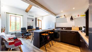 A modern kitchen with a central island, a dining area with a sofa and chairs, and a living room with a TV and bookshelves.