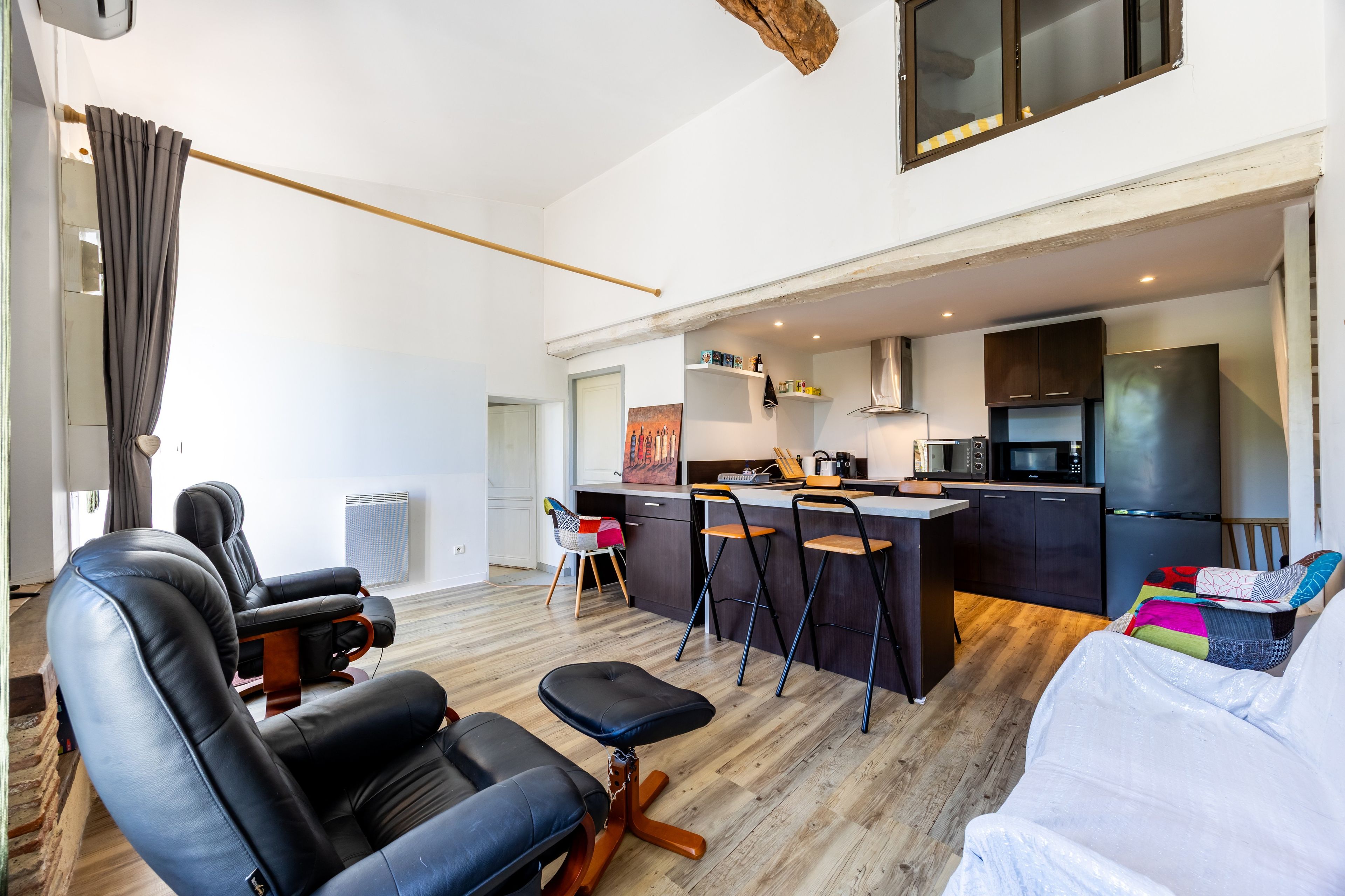 Een moderne woonkamer met een zwarte leren bank, een houten salontafel en een witte fauteuil.