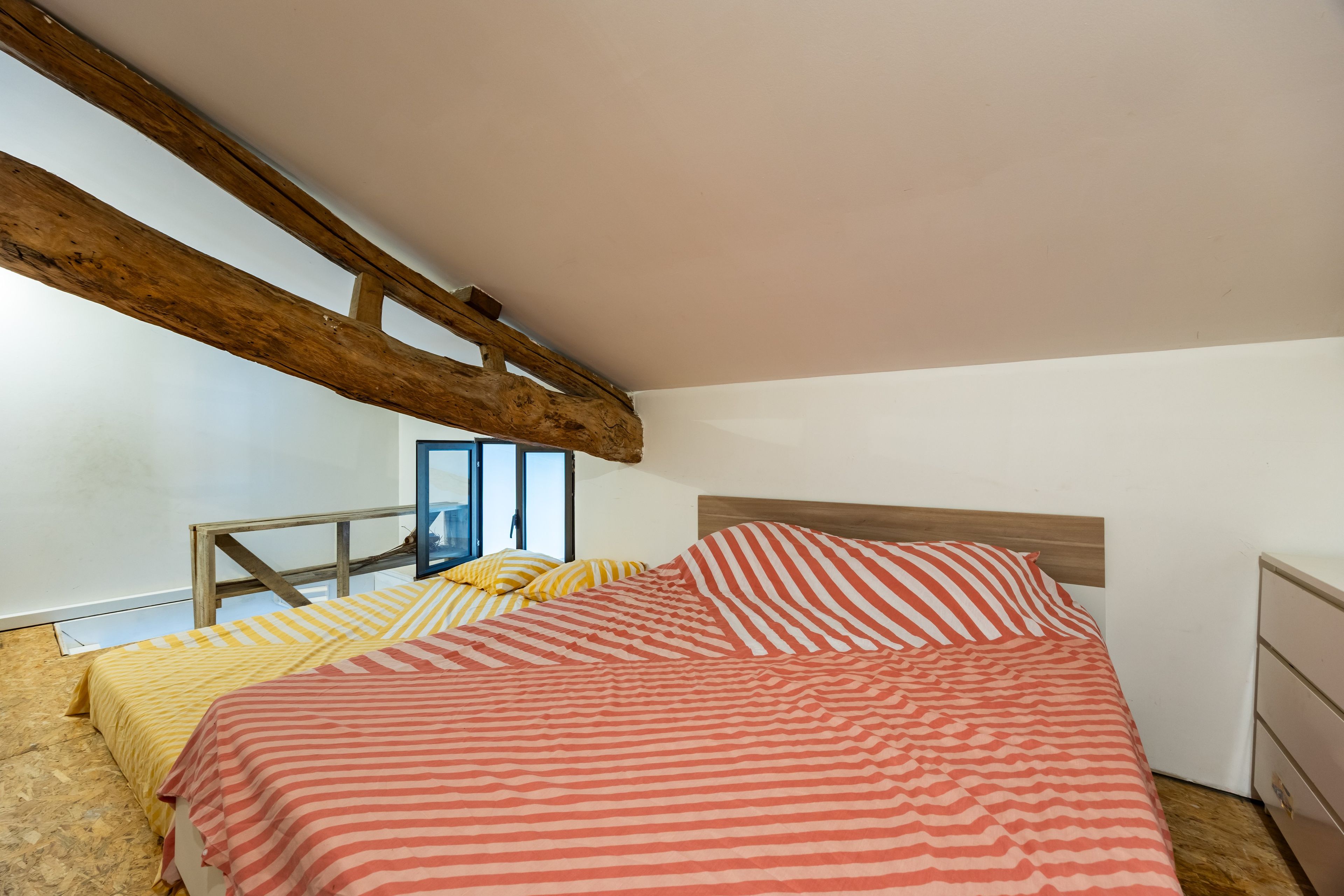 Una camera da letto con soffitto spiovente, un letto con lenzuola a righe, una testiera in legno e una finestra vista.