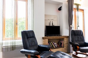 Uma sala de estar com duas poltronas de couro preto, uma televisão de tela plana e uma estante de livros.