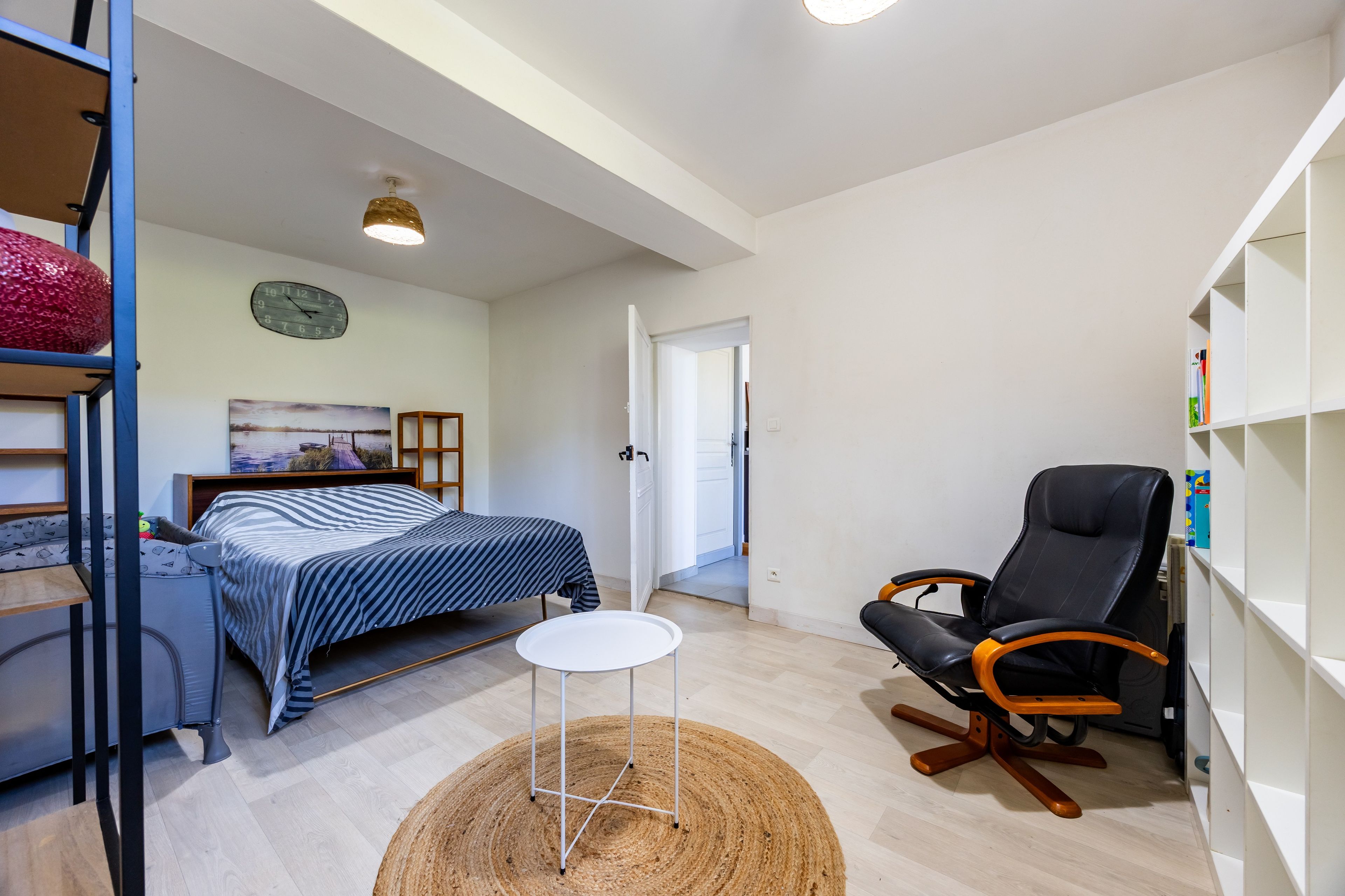 Een knusse kamer met een bed, een stoel, een klein tafeltje en een boekenplank.