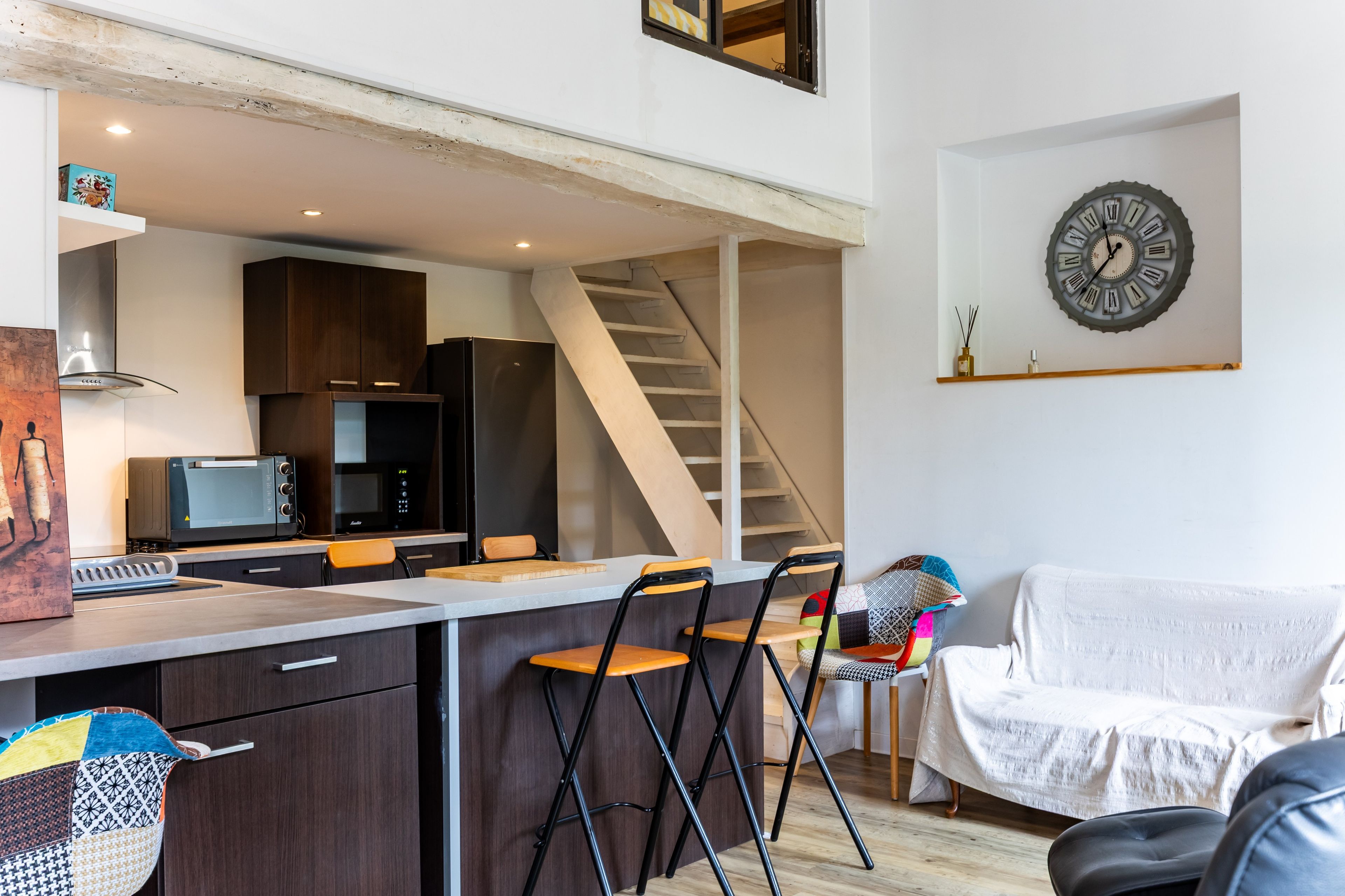 A compact living space with a kitchenette, a dining area, a sofa, and a staircase.