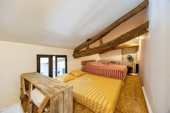 A bedroom with a wooden bed frame, a small wooden table, and a fan.