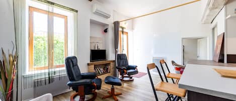 Una sala de estar moderna con chimenea, un televisor de pantalla plana y un comedor con taburetes de bar.