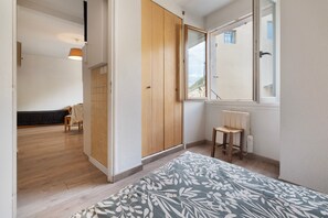 Un dormitorio con una cama, un armario de madera, un ventanal y un radiador.