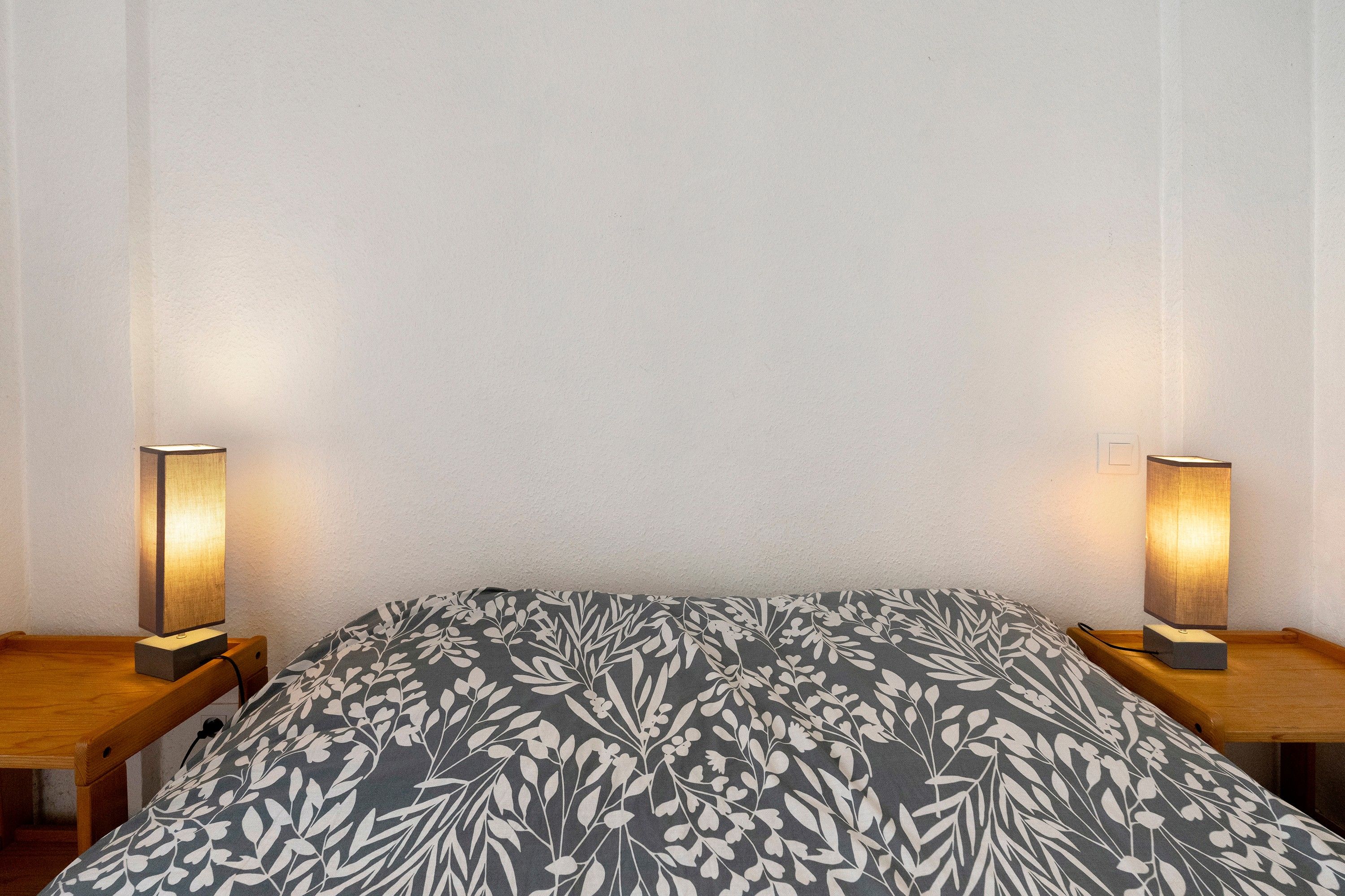 Ein Bett mit einem gemusterten Überwurf, zwei Nachttischlampen und einem Holznachttisch.