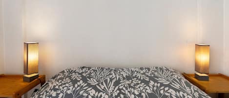Ein Bett mit einem gemusterten Überwurf, zwei Nachttischlampen und einem Holznachttisch.