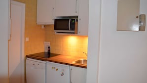 Una cocina compacta con armarios blancos, un microondas, un lavavajillas y un fregadero.