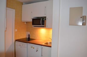 Una cocina compacta con armarios blancos, un microondas, un lavavajillas y un fregadero.