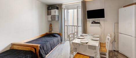 Habitación pequeña con cama, una mesita y sillas, televisor y refrigerador.