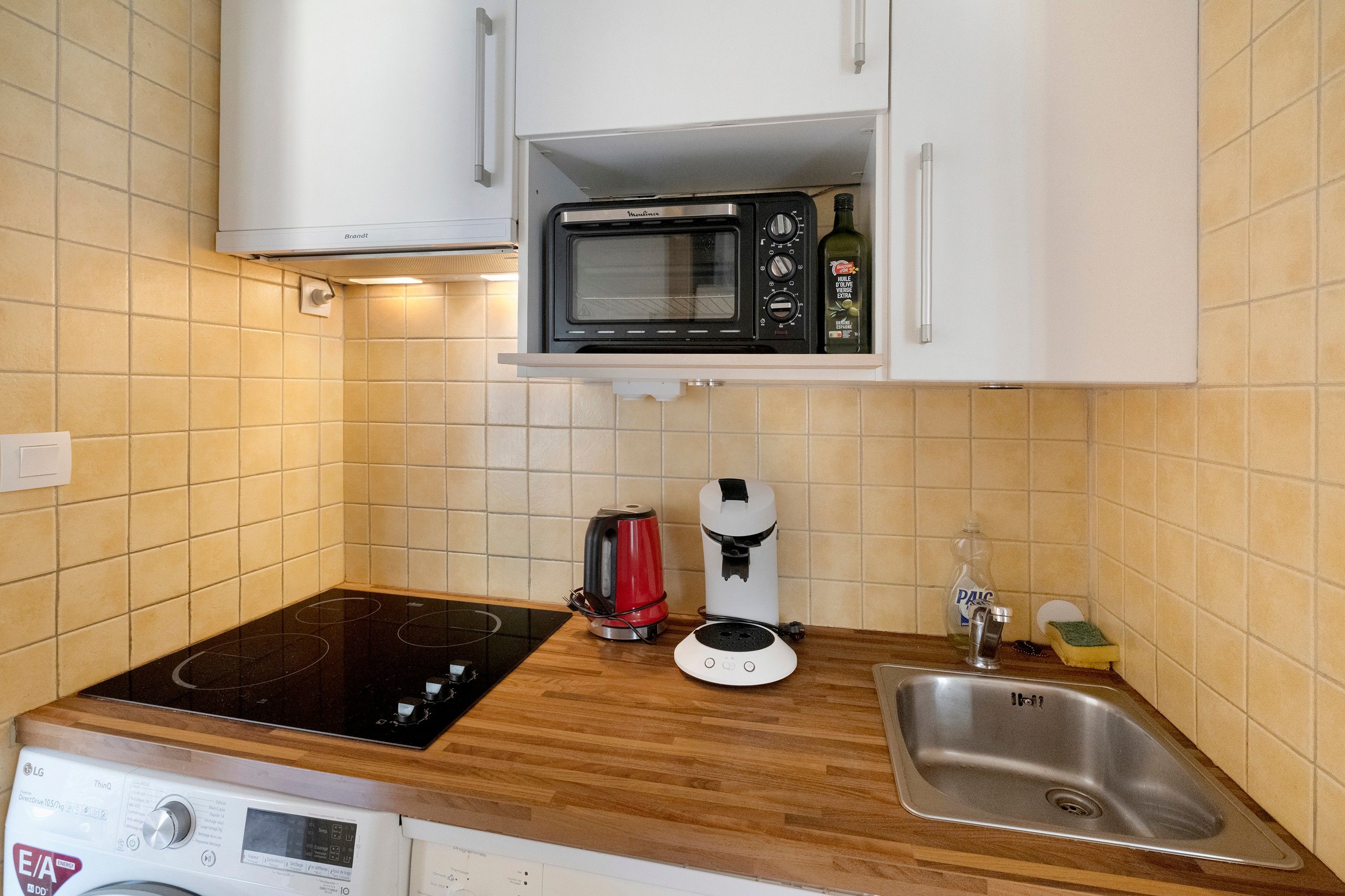 Une cuisine compacte équipée d’un four à micro-ondes encastré, d’une bouilloire, d’une machine à café et d’un lave-vaisselle.
