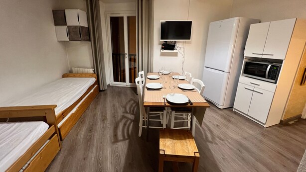 Una camera compatta con un letto, un tavolo da pranzo con sedie, un angolo cottura con forno a microonde e un televisore.