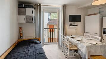 Una habitación compacta con una cama, una mesa de comedor para dos personas, un televisor y un refrigerador.