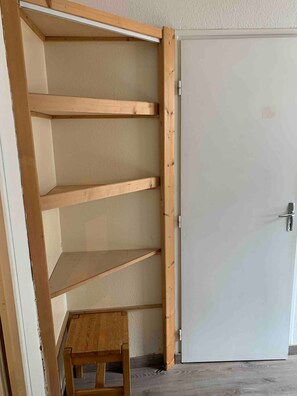 Una habitación con una estantería de madera contra la pared, un taburete pequeño de madera y una puerta blanca.