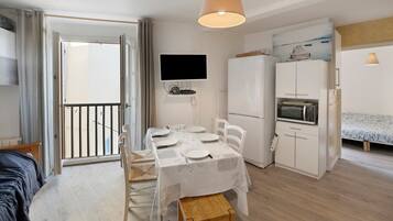 A compact living space with a dining area, a kitchenette, a TV mounted on the wall, and a balcony with a view.