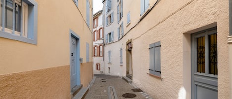 A narrow alleyway between buildings with a gravel path, doors, and windows with shutters.