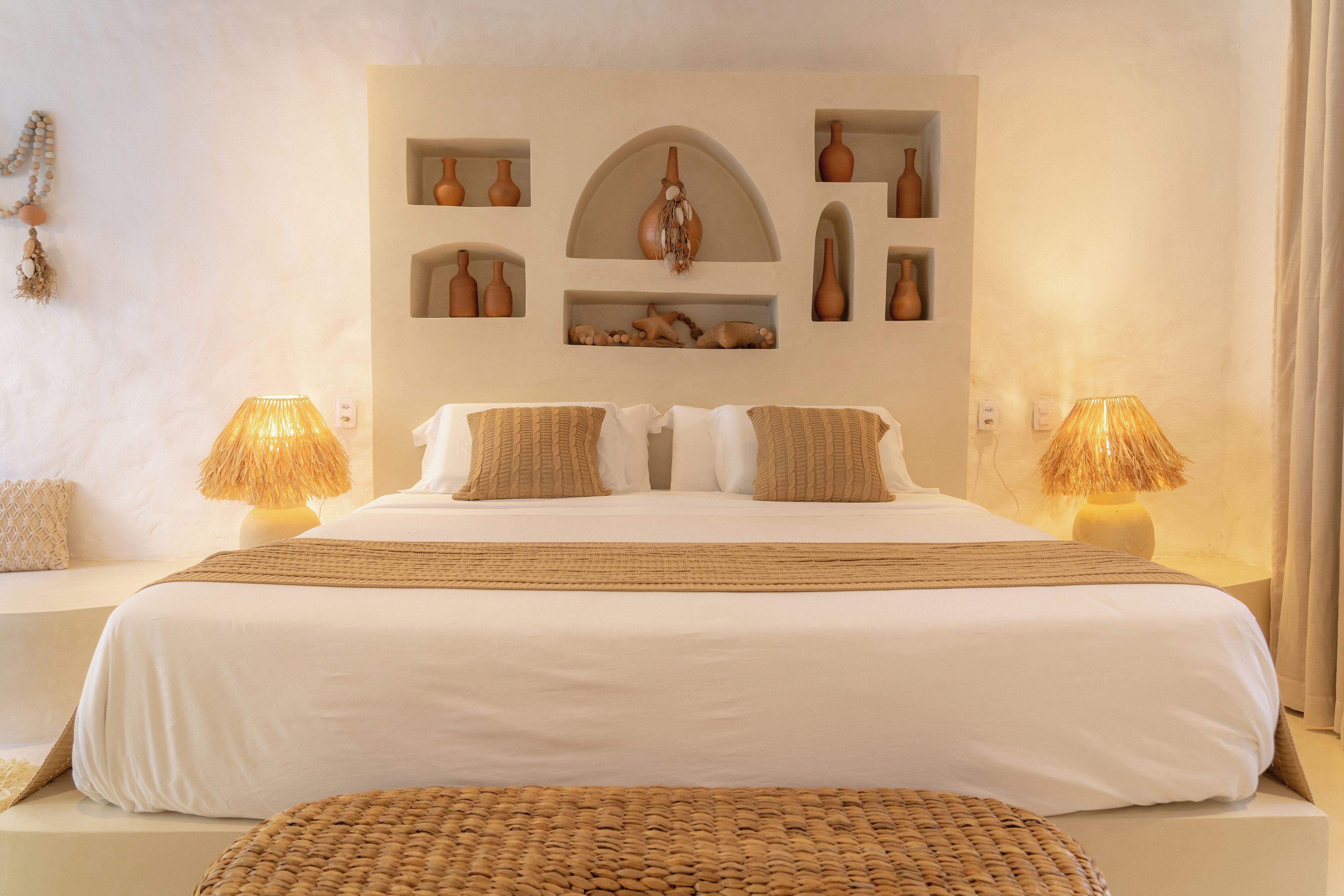 Una habitación de hotel con una cama grande, dos lámparas de noche y un estante en la pared con adornos.