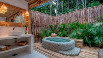 Un baño con un lavabo blanco, estantes y una bañera de piedra.