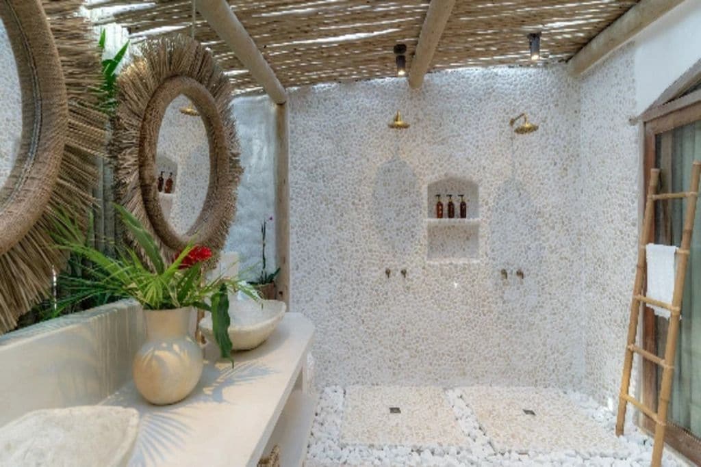 A spa area with a pebble floor, a wooden ladder, and a wall-mounted shelf with bottles.