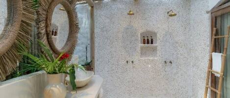 A spa area with a pebble floor, a wooden ladder, and a wall-mounted shelf with bottles.