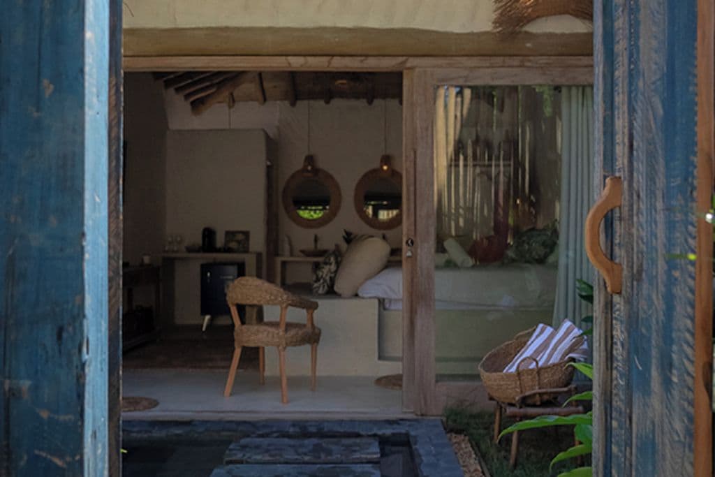 A rustic interior with a wooden door, a wicker chair, a small table, and a basket.