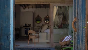 Interior rústico com porta de madeira, cadeira de vime, mesa pequena e cesta.