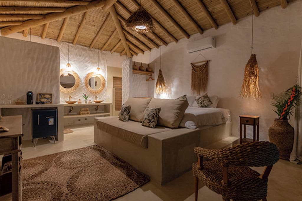 A cozy living room with a sofa, a chair, a rug, and a bed with pillows. There are hanging lights and a vase with plants.