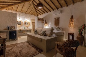 A cozy living room with a sofa, a chair, a rug, and a bed with pillows. There are hanging lights and a vase with plants.