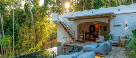 A poolside area with a wooden deck, lounge chairs, and a stone building with a staircase.