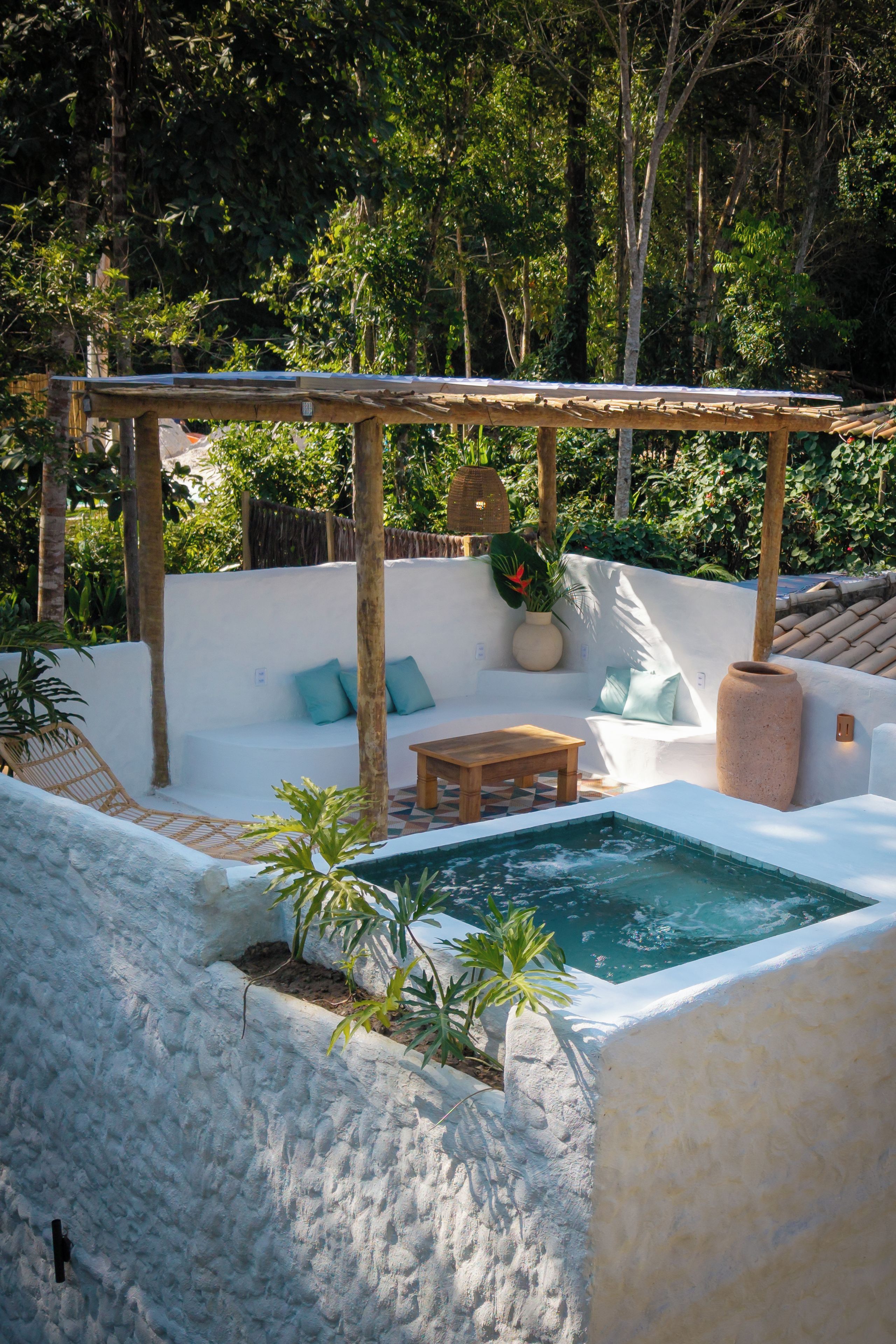 A sunlit outdoor area with a pool, a wooden table, and a white wall.