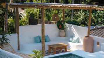 Un espacio al aire libre iluminado por el sol, con piscina, mesa de madera y pared blanca.