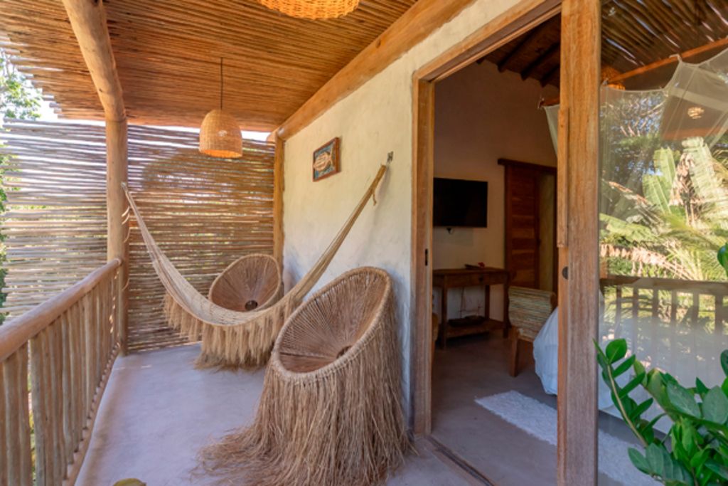 A room with a thatched roof, two woven chairs, a television, and a view of greenery outside.