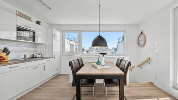 A modern kitchen with white cabinetry, a dining table with chairs, a pendant light, and a city view through large windows.